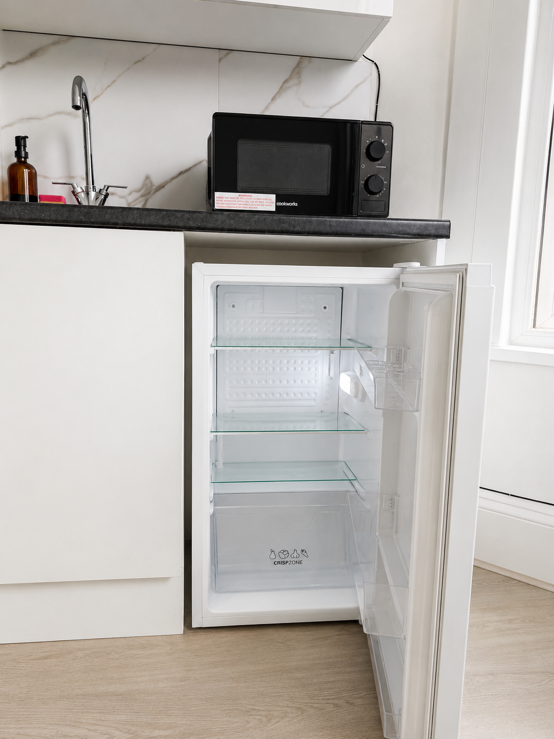 Under-counter fridge open beside the kitchen sink and microwave