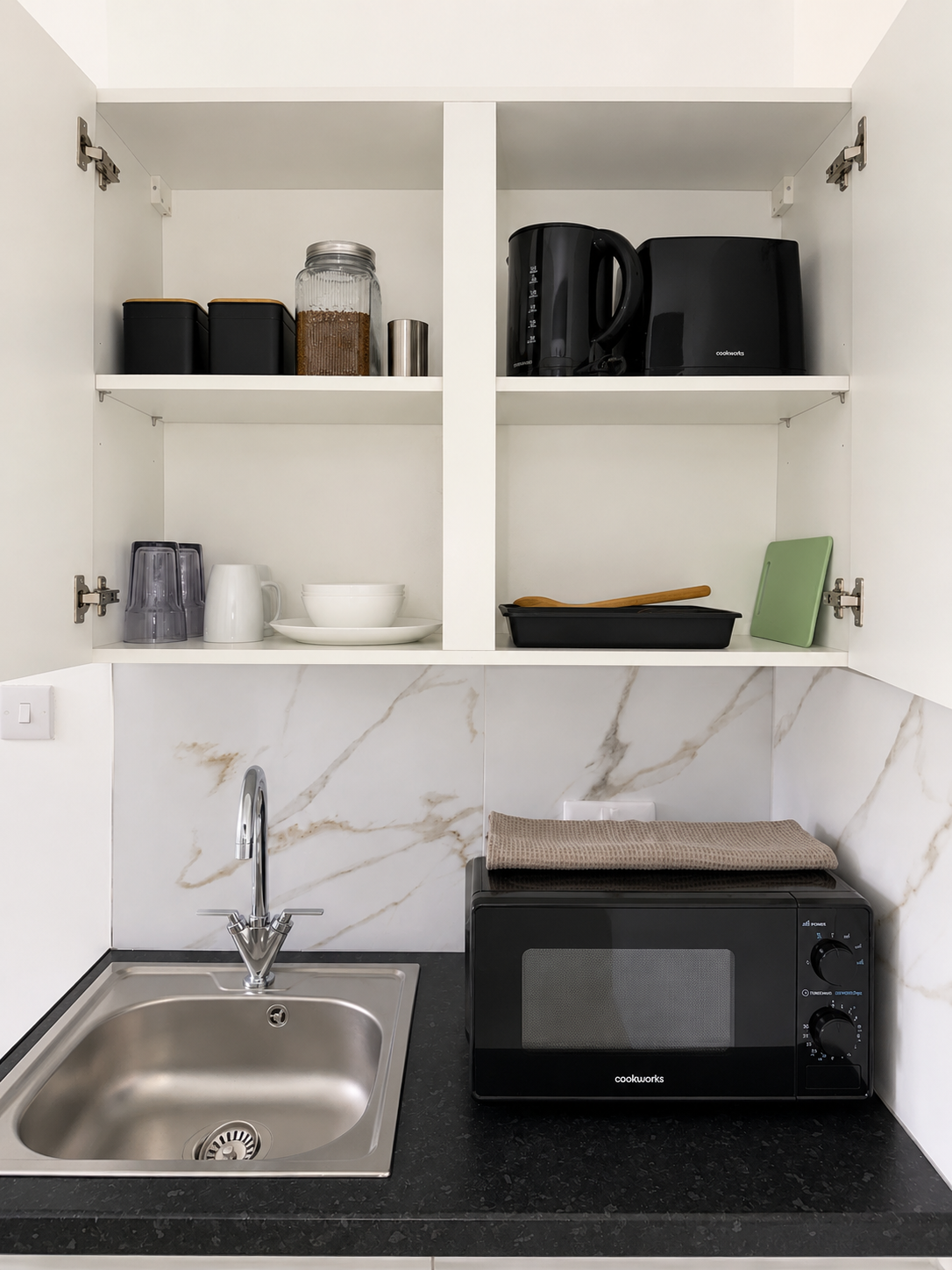 Kitchen cupboards stocked with crockery, kettle, toaster and utensils above the sink