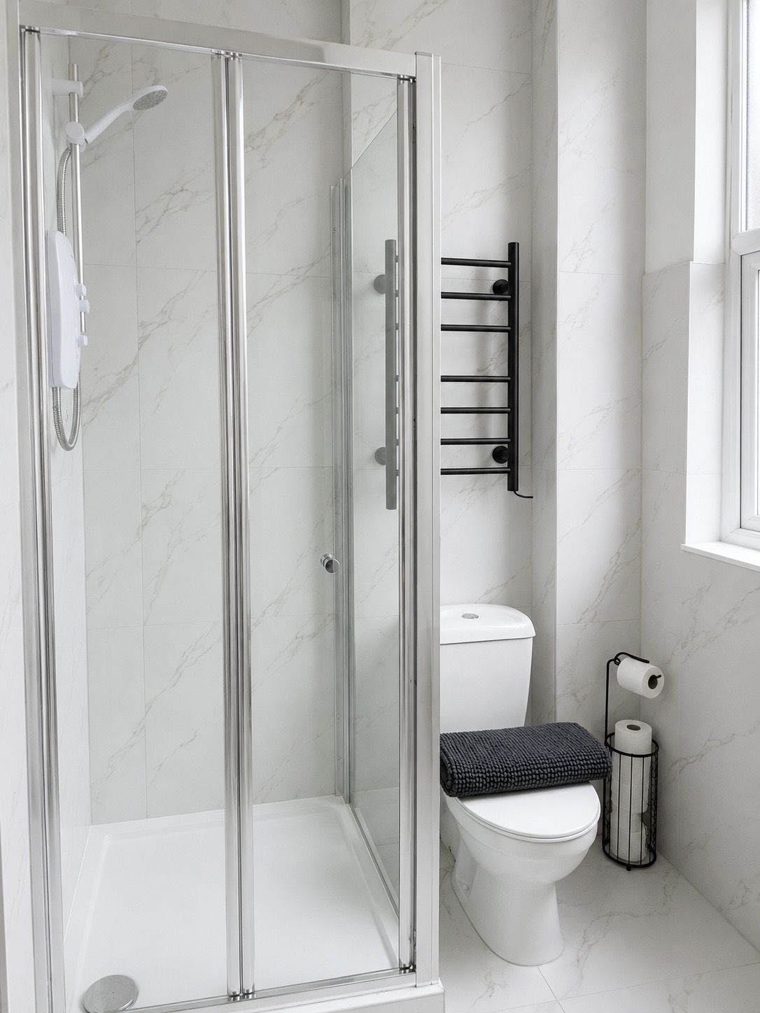 Walk-in shower enclosure with marble tiling and black towel rail