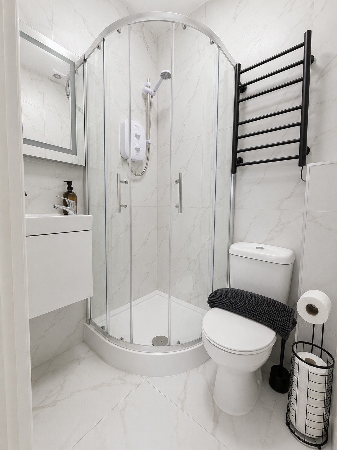 Private bathroom with marble tiling, quadrant shower, basin and heated towel rail
